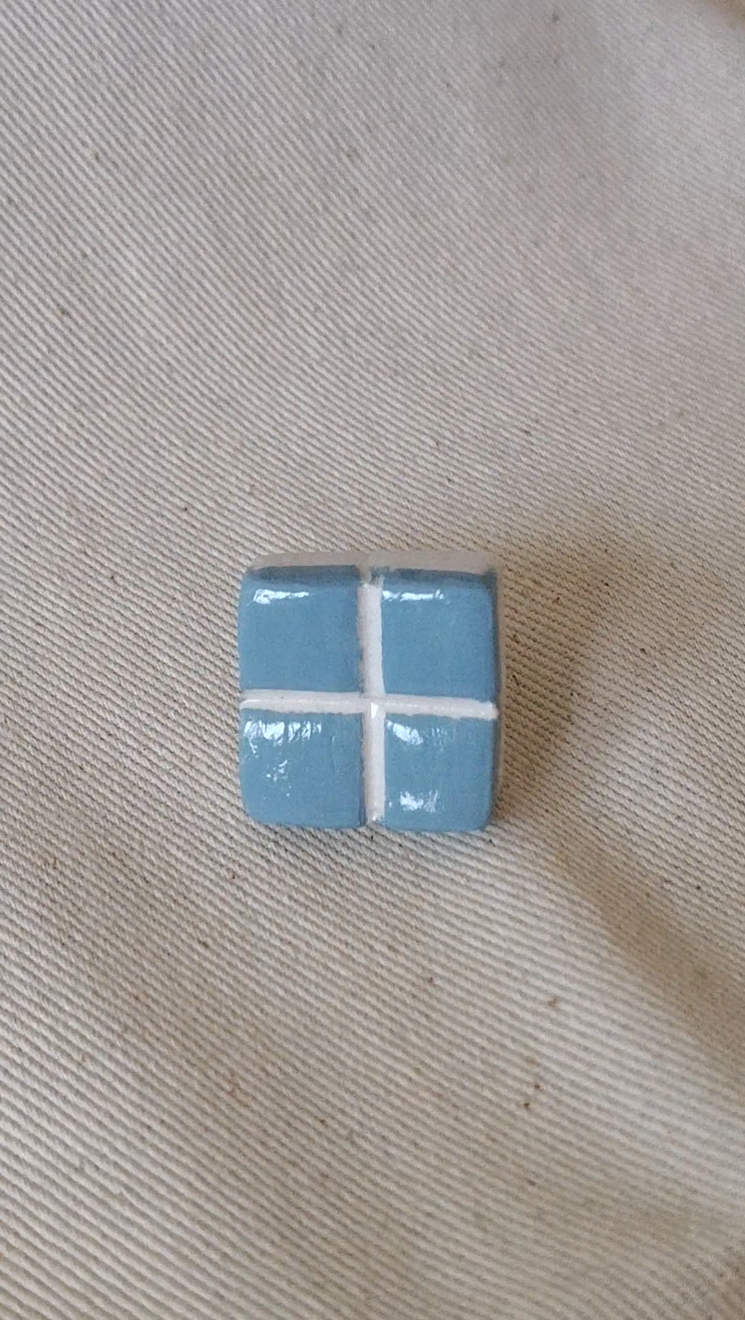 Small blue square with white cross on a beige fabric background